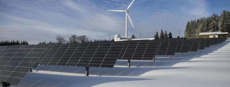 Über uns Solarpanels auf Schnee mit Windrad unter klarem Himmel