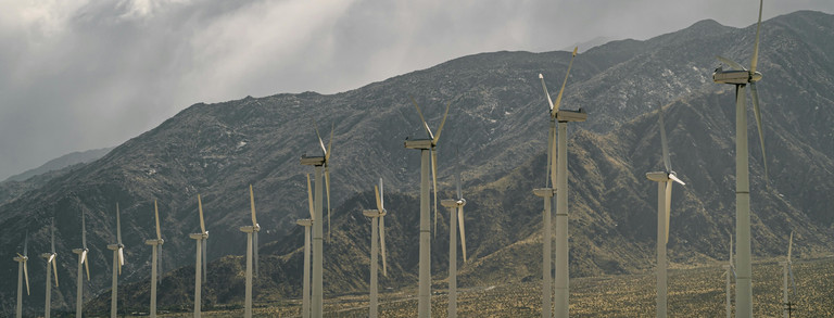 Windkraftanlagen in der Nähe von Bergen unter bewölktem Himmel